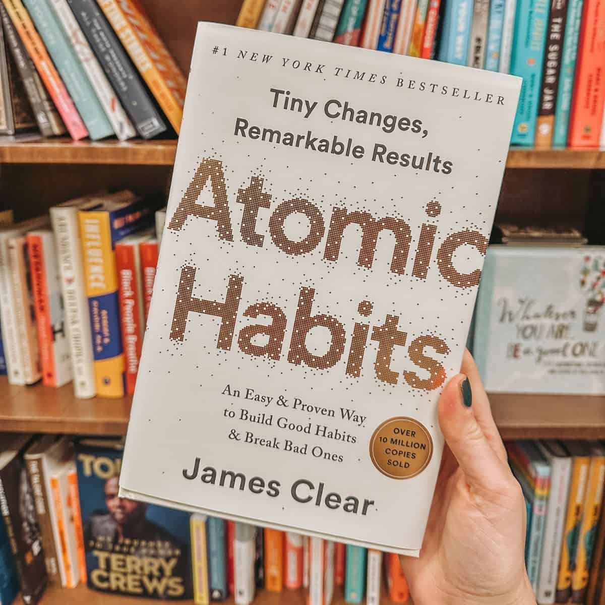 atomic habits by james clear in front of bookshelves.