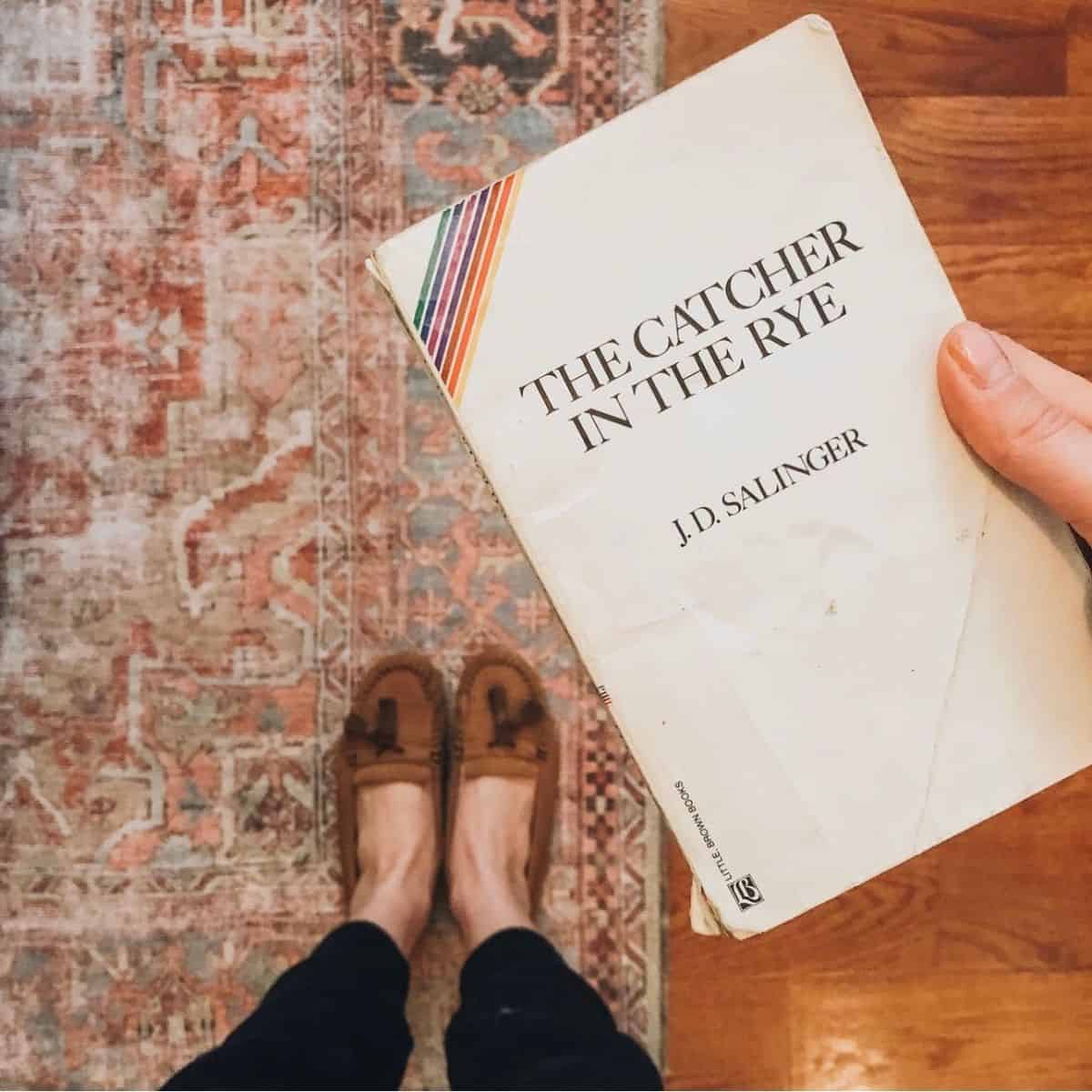 person holding the catcher in the rye by jd salinger over a rug.