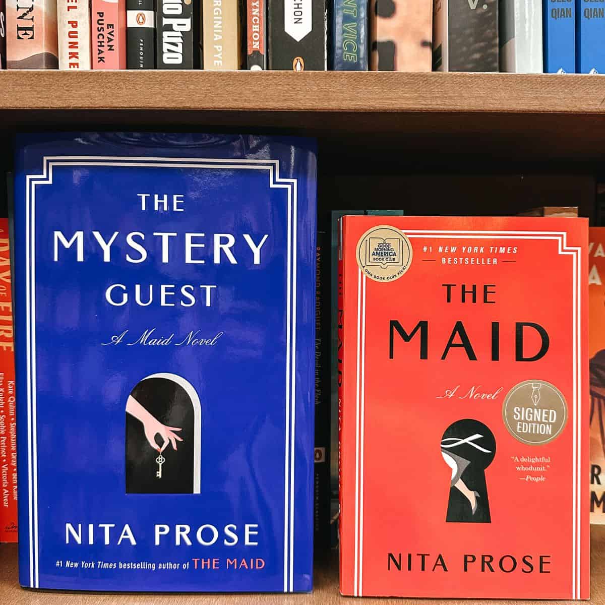 the mystery guest and the maid by nita prose in front of bookshelves.