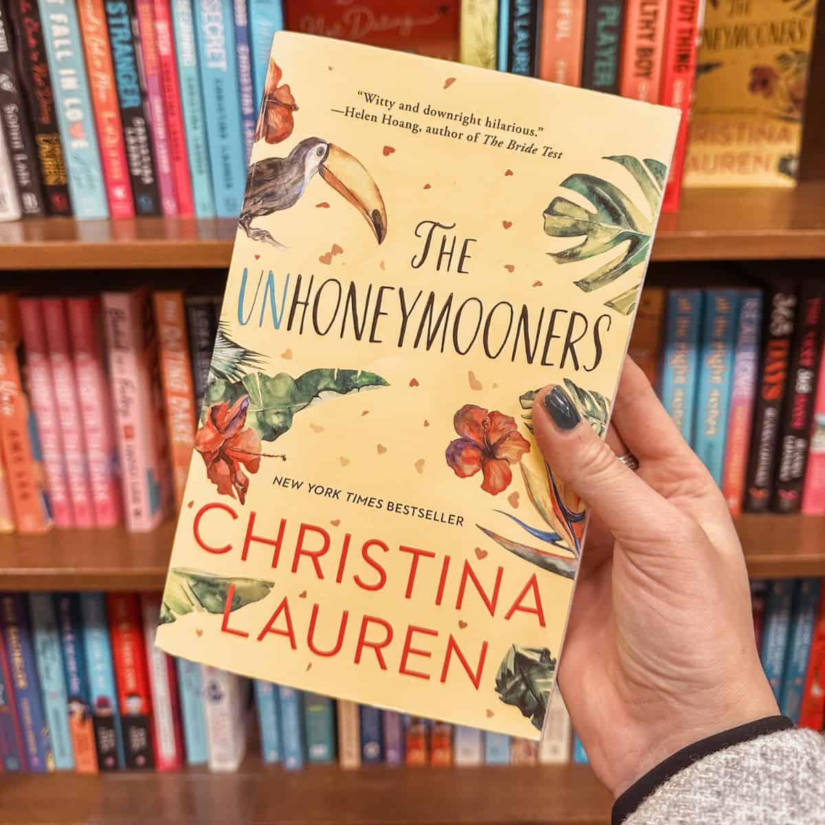 the unhoneymooners by christina lauren in front of bookshelves.