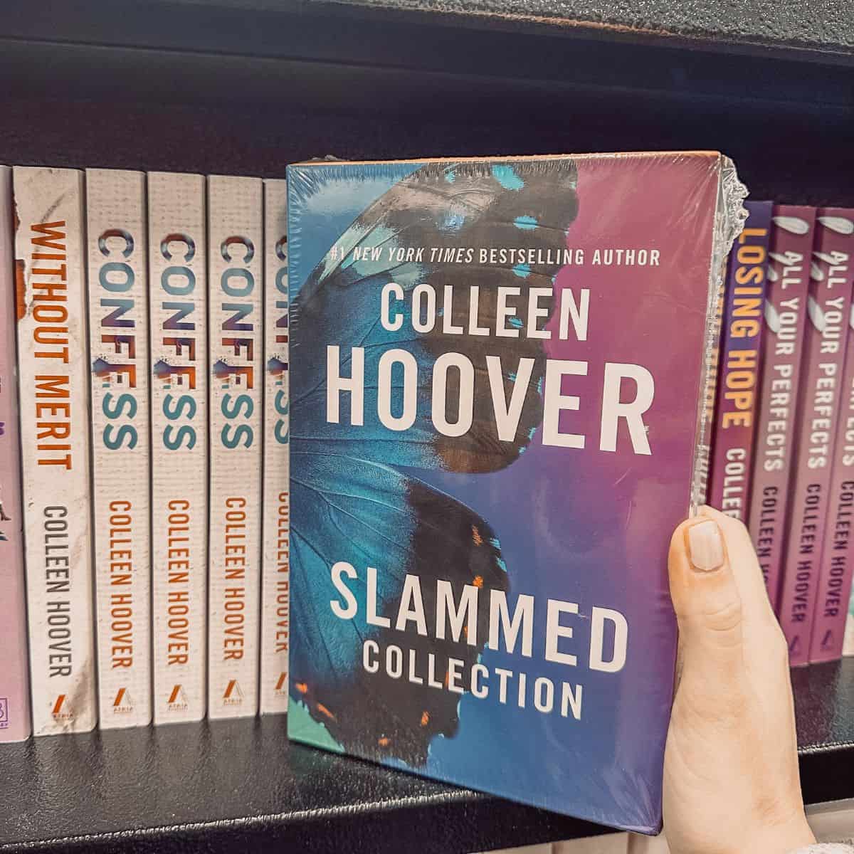 Slammed by Colleen Hoover held in front of a bookshelf with other Colleen Hoover books.