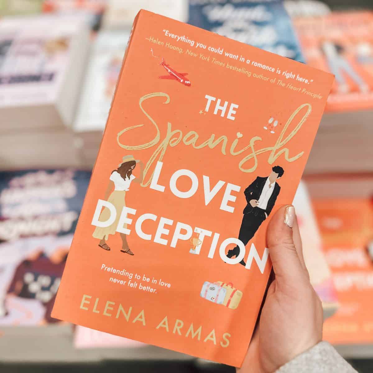 The Spanish love deception by Elena armas in front of a table of books.