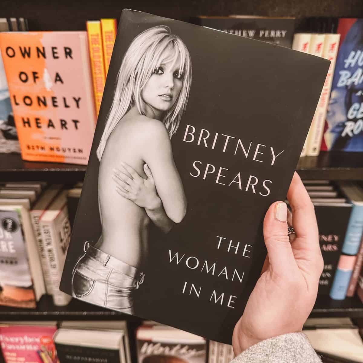 The woman in Me by Britney Spears in front of a bookshelf.