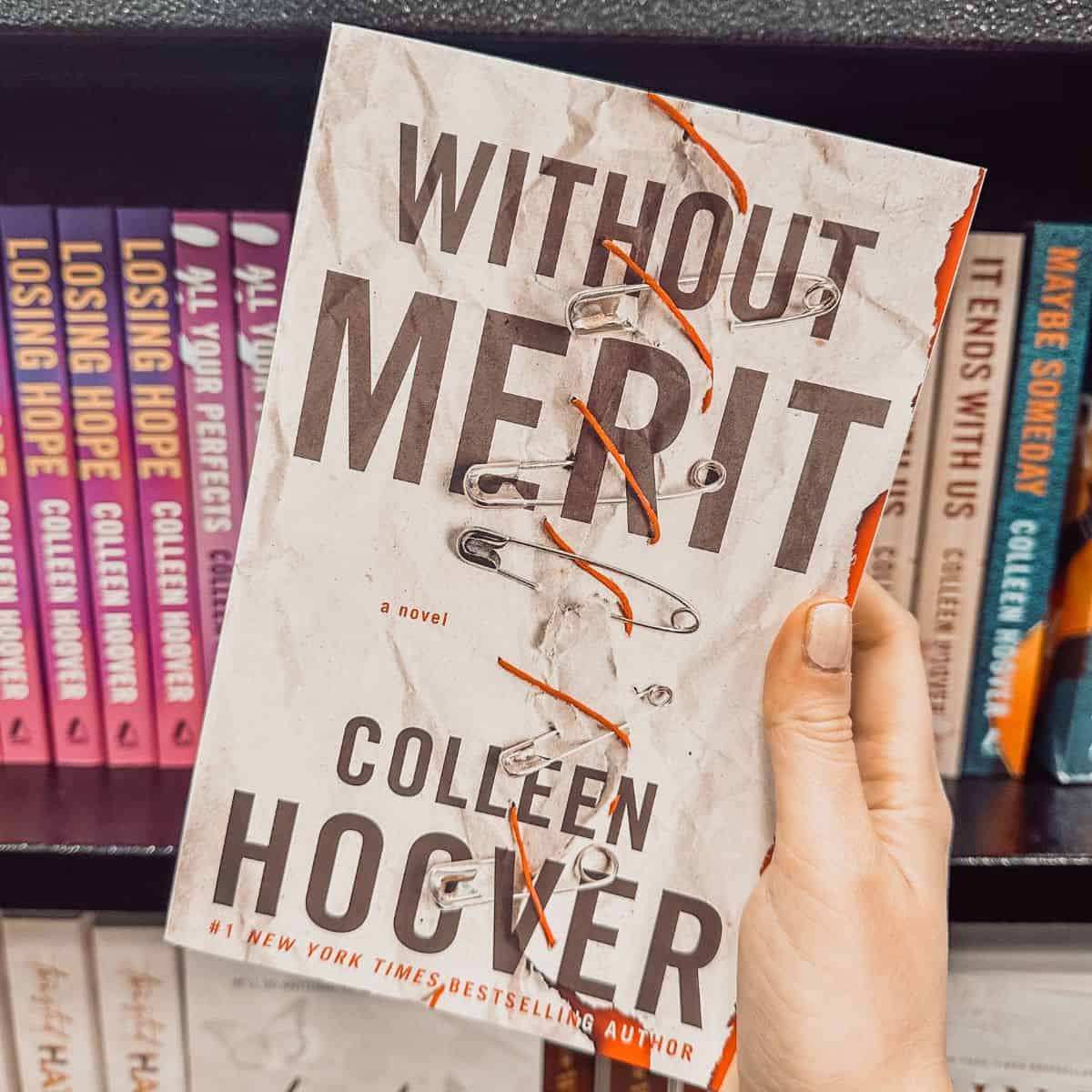 Without Merit by Colleen Hoover held in front of a bookshelf with other Colleen Hoover books.