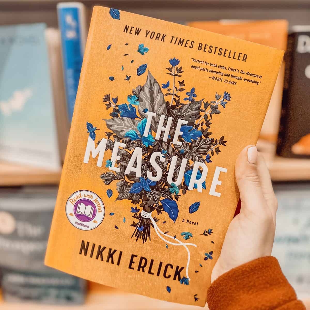 The measure by Nikki Erlick held in front of a bookshelf.