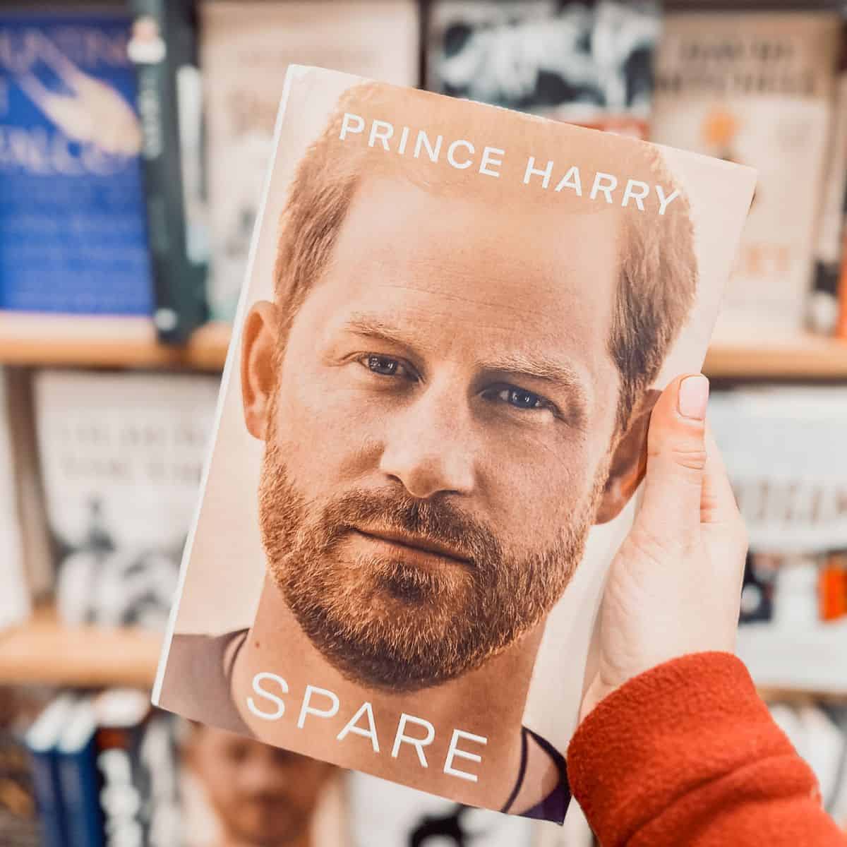 Spare by Prince Harry held in front of a bookshelf.