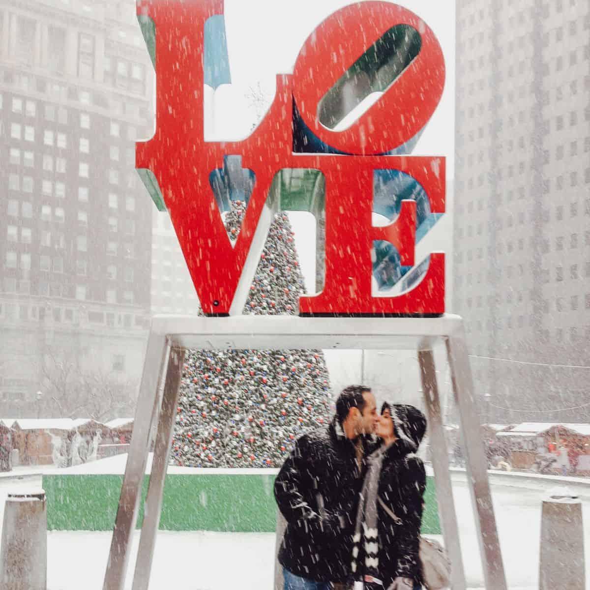 couple kissing in front of christmas tree and love sign.